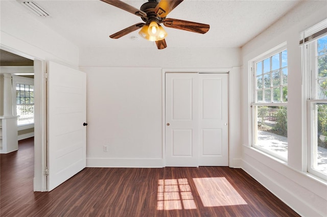 unfurnished bedroom with multiple windows, baseboards, and dark wood-style flooring