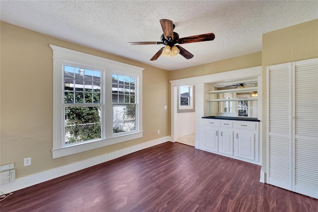 interior space featuring a textured ceiling, ceiling fan, dark wood-style flooring, and baseboards