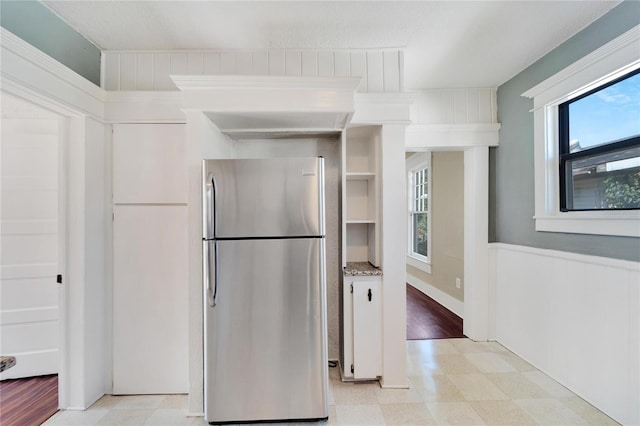 kitchen with a wainscoted wall, light stone counters, light floors, and freestanding refrigerator