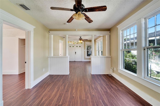 unfurnished living room with a textured ceiling, dark wood-style flooring, visible vents, and baseboards