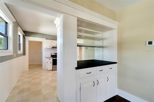 kitchen with electric range, dark countertops, a wainscoted wall, white cabinetry, and open shelves