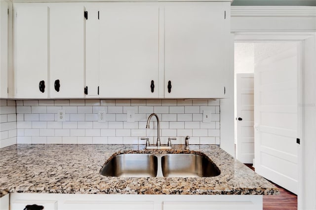 kitchen with light stone countertops, white cabinetry, and a sink