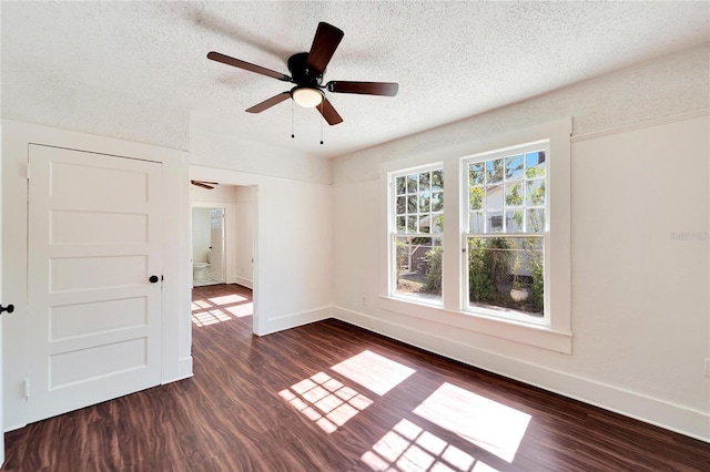 empty room with a textured ceiling, ceiling fan, dark wood-style flooring, and baseboards