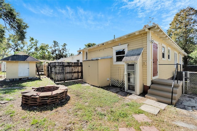 rear view of property featuring a fire pit, a storage unit, an outdoor structure, and fence