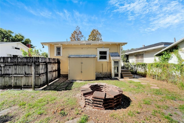 rear view of house featuring a fire pit, a storage unit, an outdoor structure, and a fenced backyard