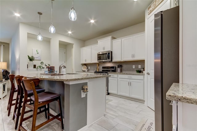 kitchen with appliances with stainless steel finishes, hanging light fixtures, a kitchen island with sink, and white cabinetry