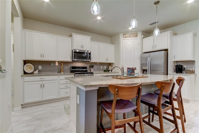 kitchen with appliances with stainless steel finishes, decorative backsplash, white cabinetry, and a center island with sink