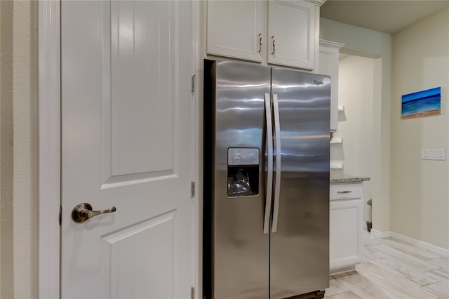 kitchen with stainless steel refrigerator with ice dispenser, white cabinets, light stone countertops, and light wood-type flooring