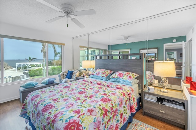 bedroom featuring a textured ceiling, a water view, hardwood / wood-style flooring, and ceiling fan