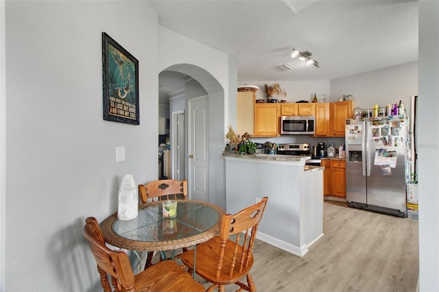 kitchen with light brown cabinets, light wood-type flooring, stainless steel appliances, and a textured ceiling