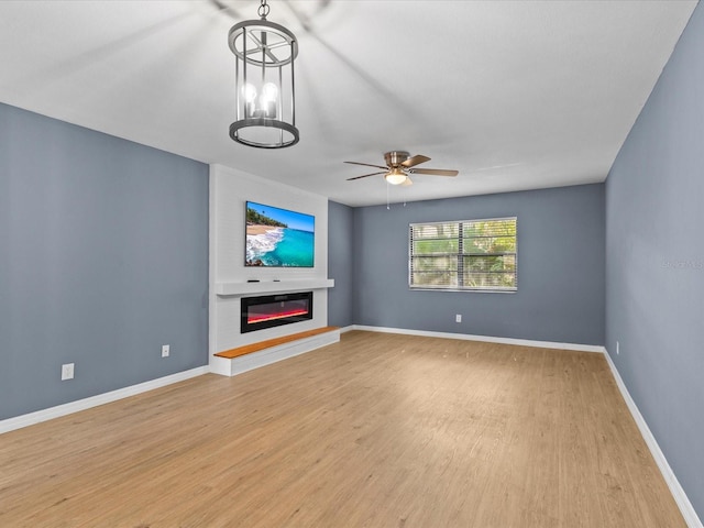 unfurnished living room with ceiling fan with notable chandelier and light wood-type flooring