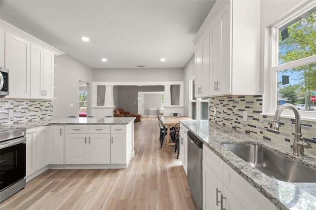 kitchen featuring appliances with stainless steel finishes, backsplash, light hardwood / wood-style flooring, white cabinets, and ornate columns