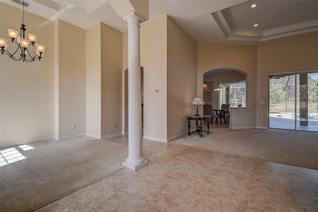 interior space with a towering ceiling, a tray ceiling, an inviting chandelier, and decorative columns