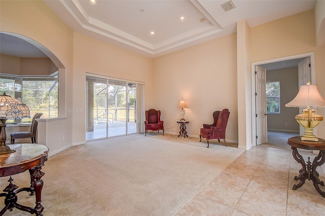 sitting room with a towering ceiling, light colored carpet, plenty of natural light, and a tray ceiling