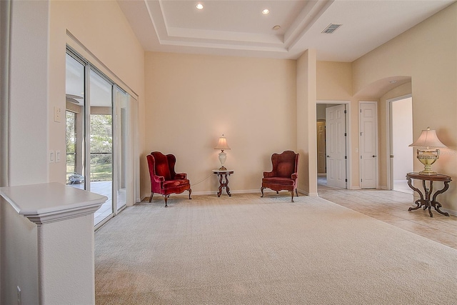 sitting room featuring a towering ceiling, light carpet, and a raised ceiling