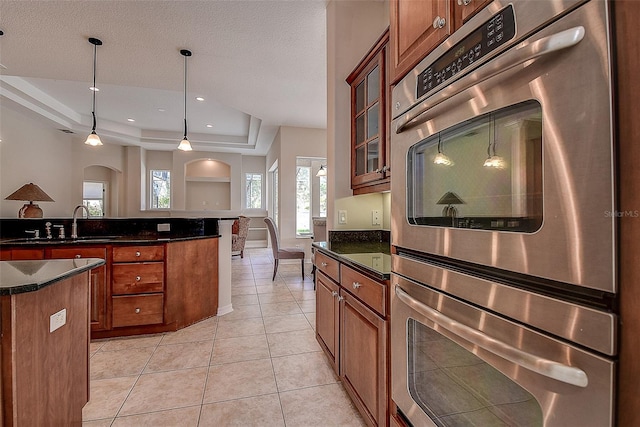 kitchen with hanging light fixtures, double oven, a kitchen island, and a tray ceiling