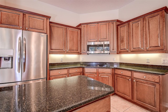 kitchen with stainless steel appliances, light tile patterned flooring, a textured ceiling, and dark stone counters