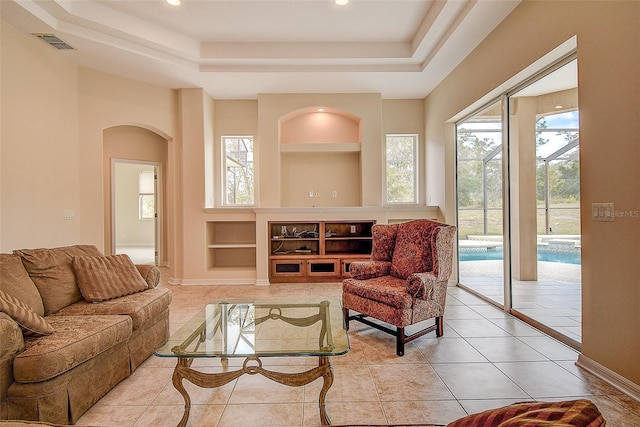 living room featuring built in features, light tile patterned floors, and a tray ceiling