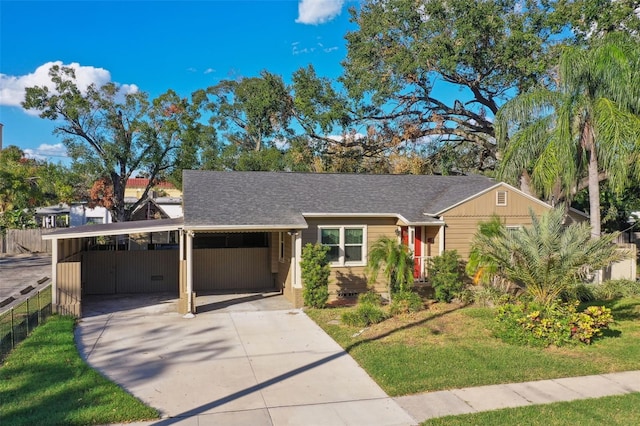 view of front facade featuring driveway, roof with shingles, fence, a carport, and a front yard