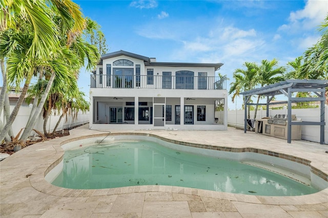 back of property featuring a balcony, a patio, a swimming pool with hot tub, and exterior kitchen