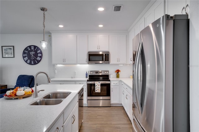 kitchen featuring stainless steel appliances, light hardwood / wood-style floors, white cabinetry, sink, and pendant lighting