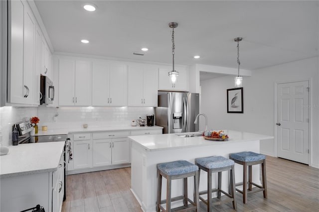 kitchen featuring stainless steel appliances, white cabinets, sink, an island with sink, and decorative light fixtures