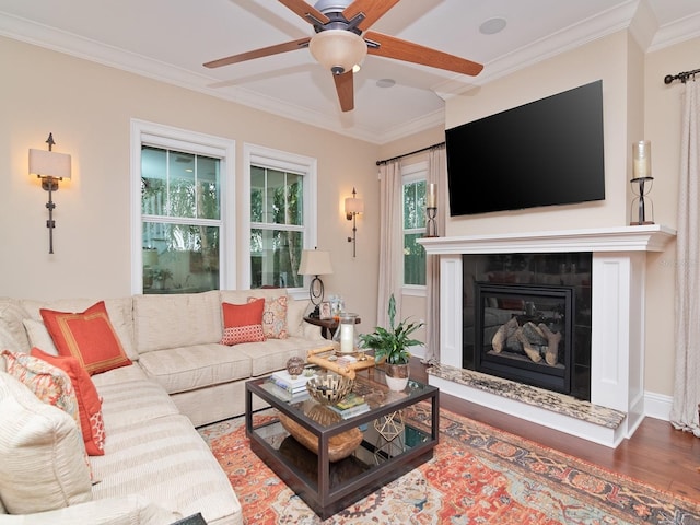 living room with ceiling fan, a tile fireplace, wood finished floors, baseboards, and crown molding