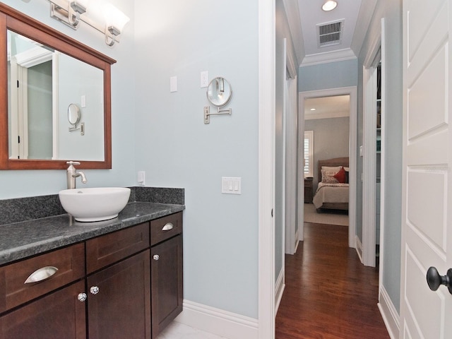 ensuite bathroom with baseboards, visible vents, wood finished floors, crown molding, and vanity