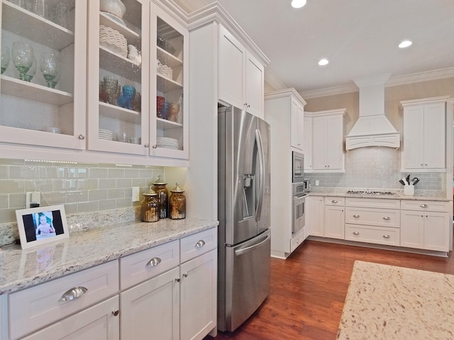 kitchen with dark wood finished floors, appliances with stainless steel finishes, ornamental molding, white cabinetry, and premium range hood