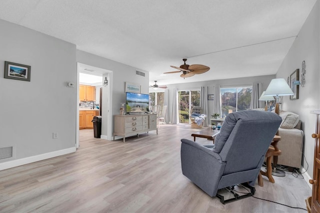 living room featuring a textured ceiling, light wood-type flooring, and ceiling fan