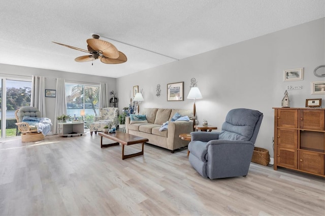 living room with a textured ceiling, light wood-type flooring, and ceiling fan