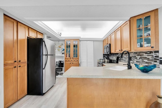 kitchen with kitchen peninsula, appliances with stainless steel finishes, backsplash, light wood-type flooring, and a tray ceiling