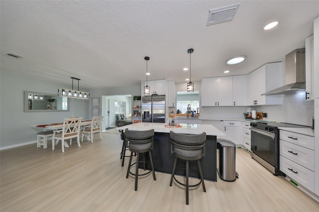 kitchen with stainless steel appliances, light hardwood / wood-style floors, wall chimney range hood, a kitchen island, and white cabinetry