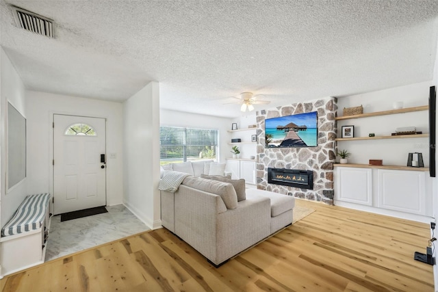 living room featuring a fireplace, light hardwood / wood-style floors, a textured ceiling, and ceiling fan