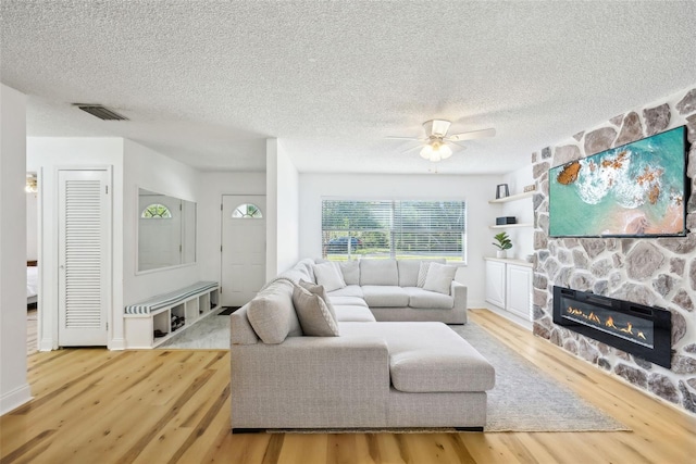 living room with a textured ceiling, a fireplace, wood-type flooring, and ceiling fan