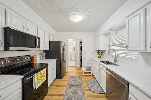 kitchen with appliances with stainless steel finishes, a textured ceiling, sink, white cabinets, and light hardwood / wood-style flooring