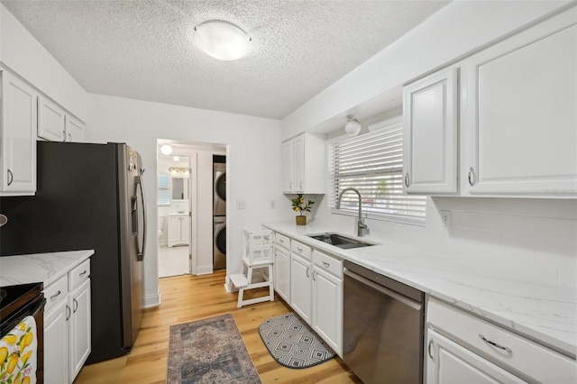 kitchen with white cabinets, stacked washing maching and dryer, light hardwood / wood-style flooring, sink, and appliances with stainless steel finishes