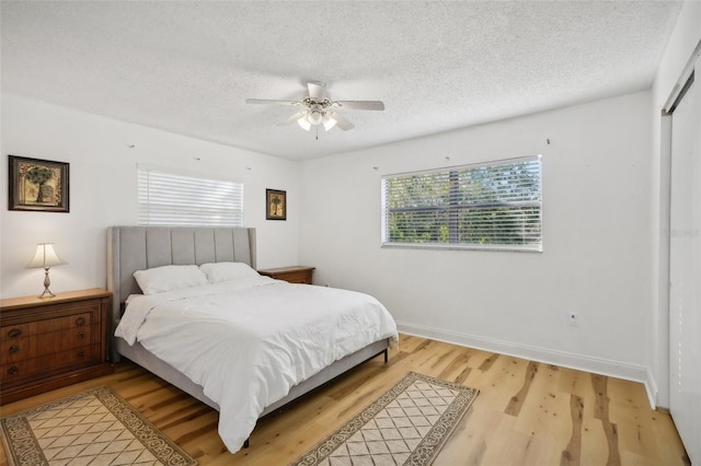 bedroom with a textured ceiling, light wood-type flooring, ceiling fan, and a closet