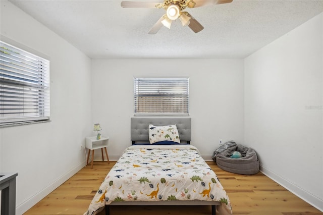 bedroom with a textured ceiling, wood-type flooring, multiple windows, and ceiling fan