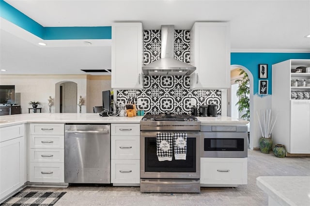 kitchen featuring stainless steel appliances, wall chimney exhaust hood, white cabinets, and decorative backsplash