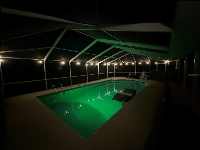 pool at night with glass enclosure, a patio area, and an outdoor pool