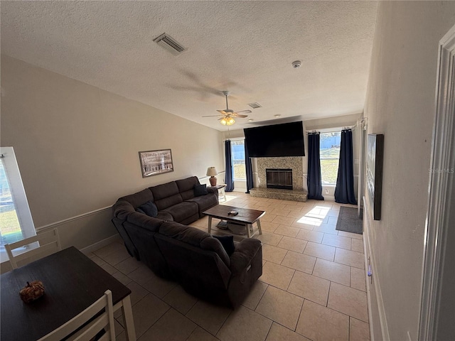 living area with a ceiling fan, visible vents, lofted ceiling, light tile patterned flooring, and a fireplace