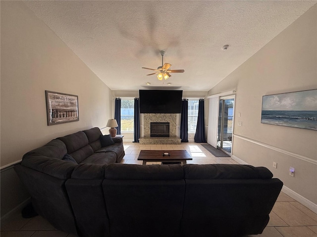 living area with a stone fireplace, vaulted ceiling, a textured ceiling, and ceiling fan