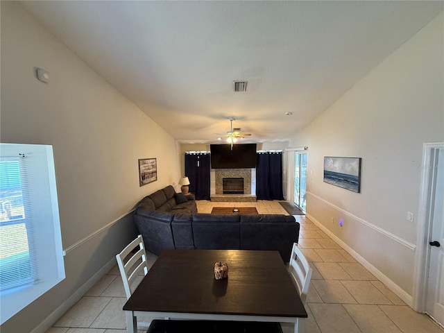 dining space featuring a ceiling fan, visible vents, lofted ceiling, light tile patterned flooring, and a stone fireplace