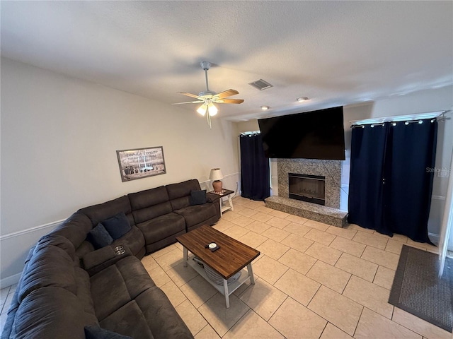 living area featuring a ceiling fan, visible vents, baseboards, light tile patterned flooring, and a fireplace with raised hearth