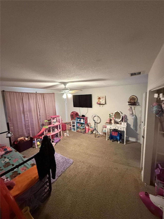 playroom featuring visible vents, a textured ceiling, carpet flooring, and a ceiling fan