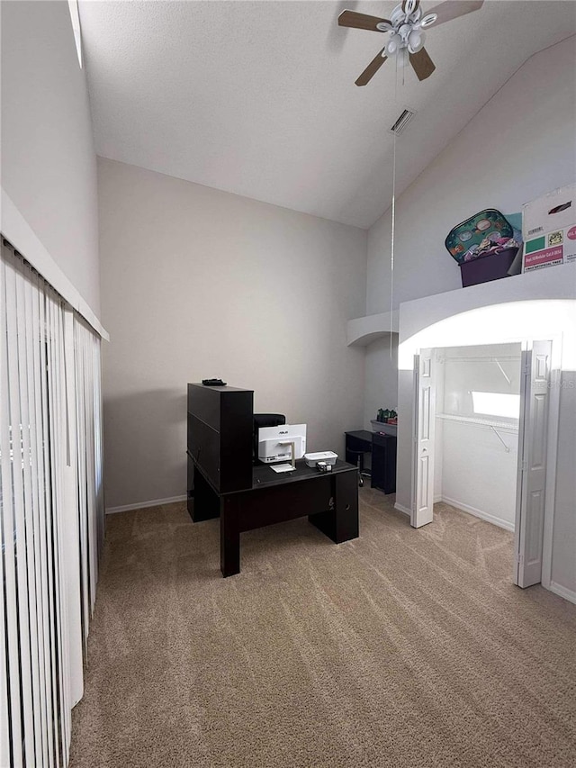 carpeted office space with ceiling fan, visible vents, baseboards, and high vaulted ceiling