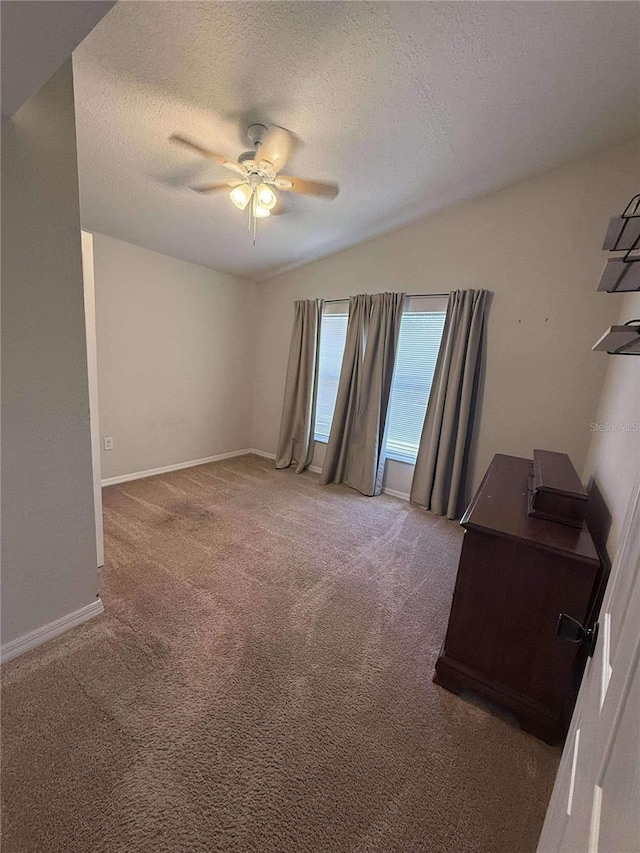 unfurnished room featuring baseboards, lofted ceiling, carpet floors, a textured ceiling, and a ceiling fan