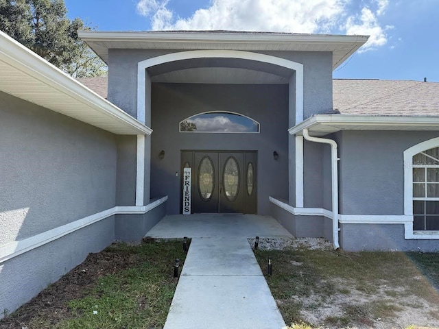 property entrance with stucco siding and a shingled roof