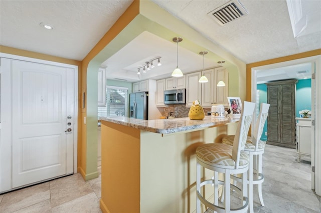 kitchen featuring pendant lighting, a breakfast bar area, decorative backsplash, light stone counters, and stainless steel appliances